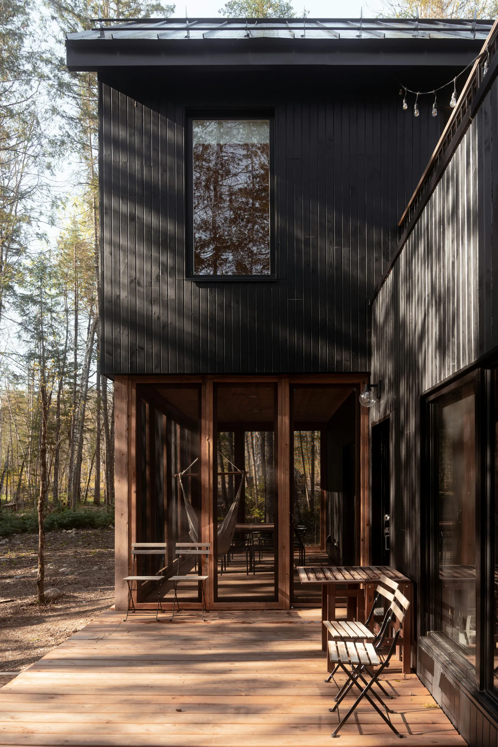 Casa de madera negra en el bosque con terraza y sillas